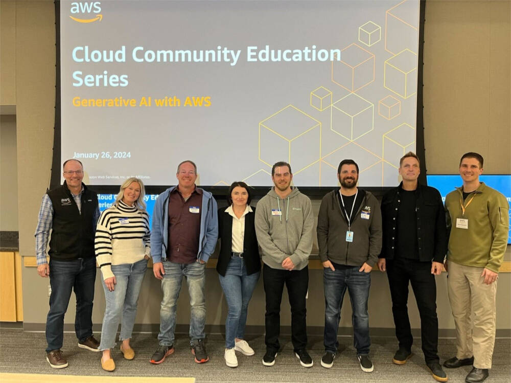 A group of eight people standing in front of a large presentation screen displaying the title "Cloud Community Education Series: Generative AI with AWS" dated January 26, 2024. The individuals are smiling and posing for the photo.